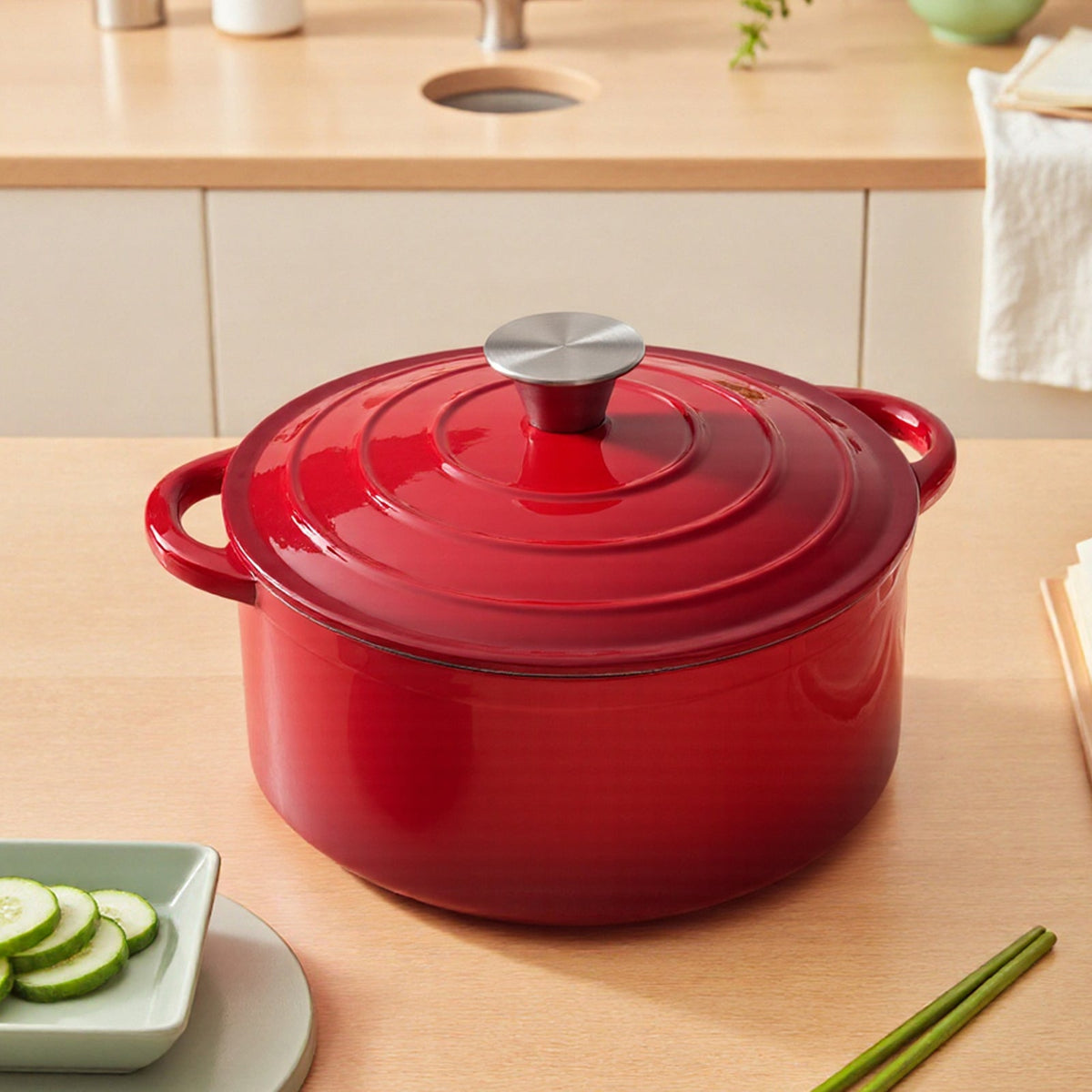 Red enamelled cast iron Dutch oven with its lid on, on a wooden kitchen worktop