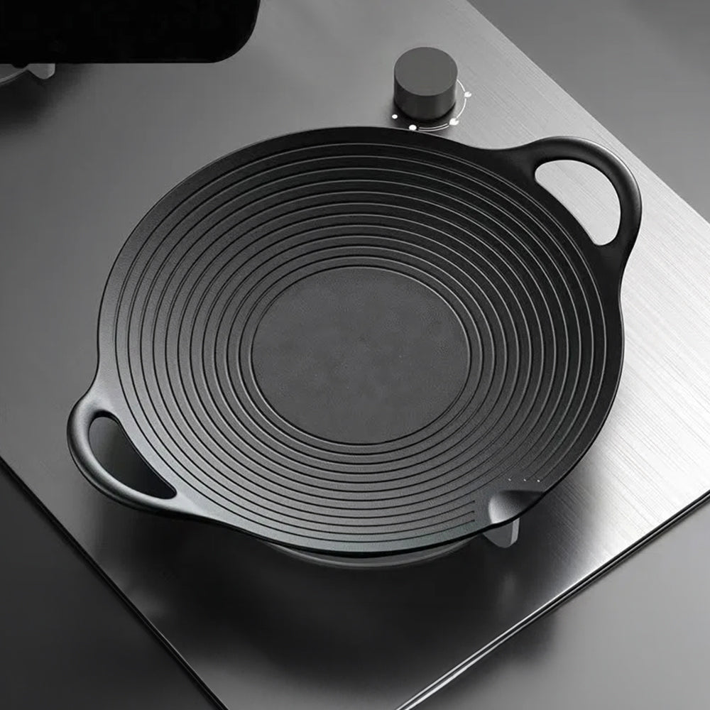Empty round cast iron grill pan on a steel hob, showing the raised rings, loop handles and spout