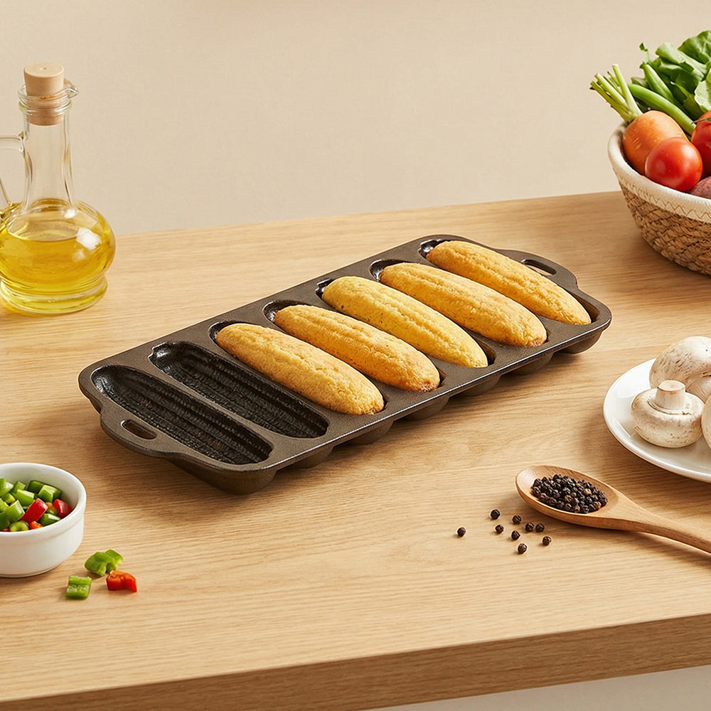 Cornbread pan with five baked corn sticks on a wooden worktop beside vegetables