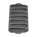Empty cast iron cornbread pan with seven corn cob moulds and two end handles on white
