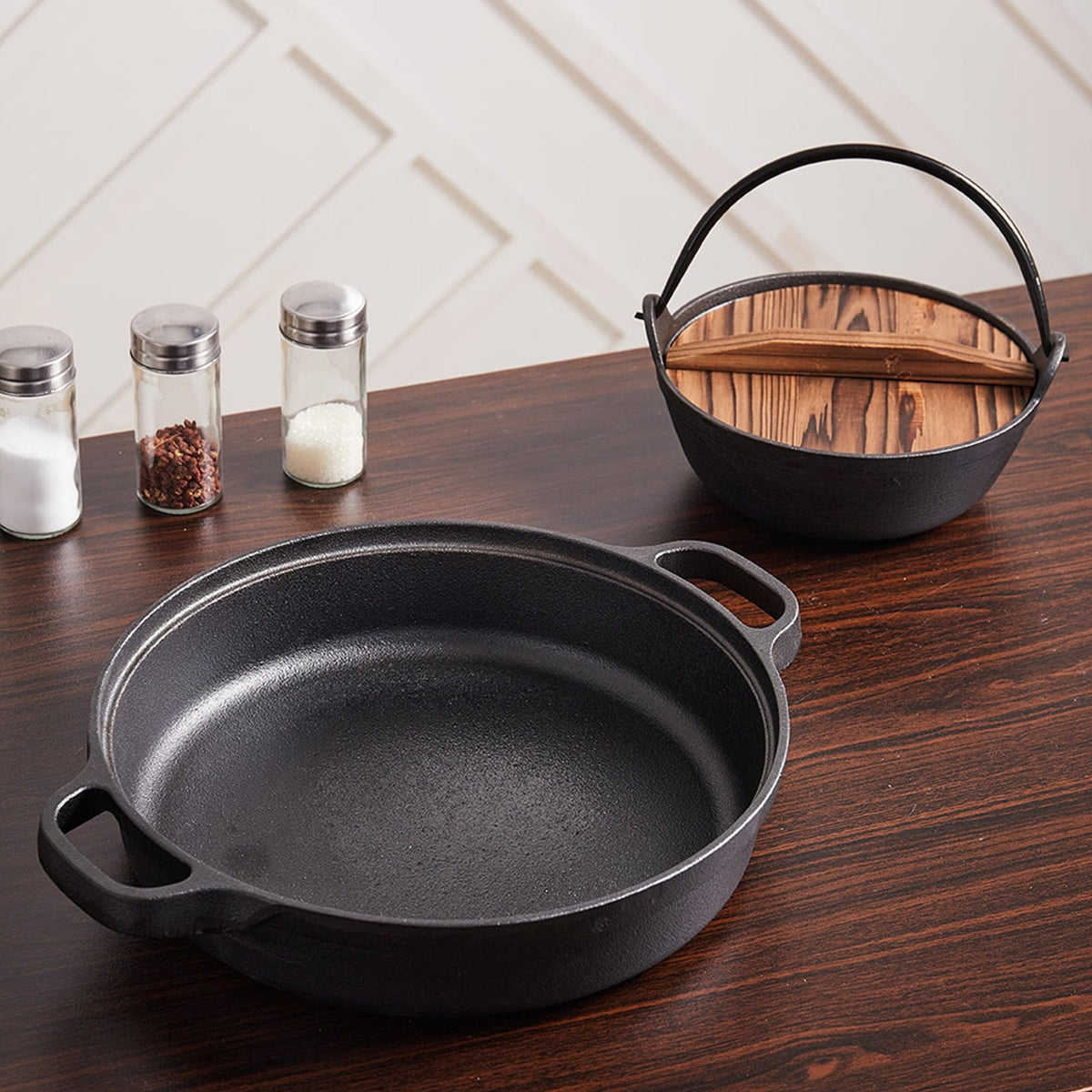Empty two-handled cast iron skillet on a dark wooden table, another pot behind it