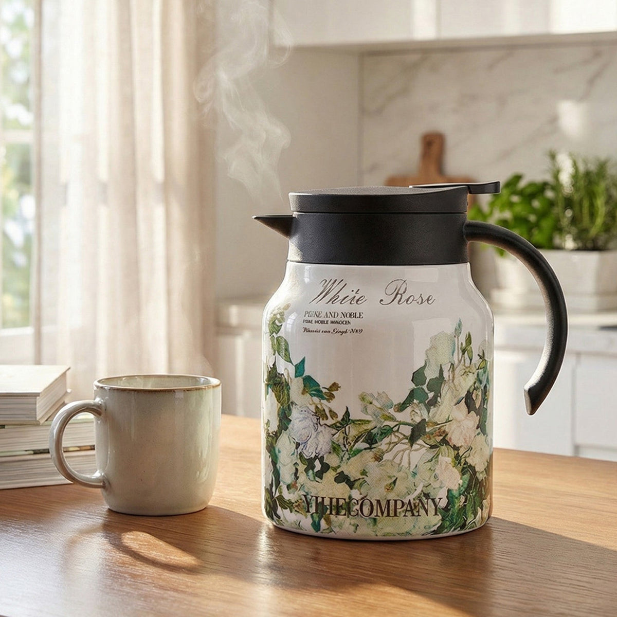 White thermal teapot printed with green leaves and white roses, beside a mug on a kitchen table