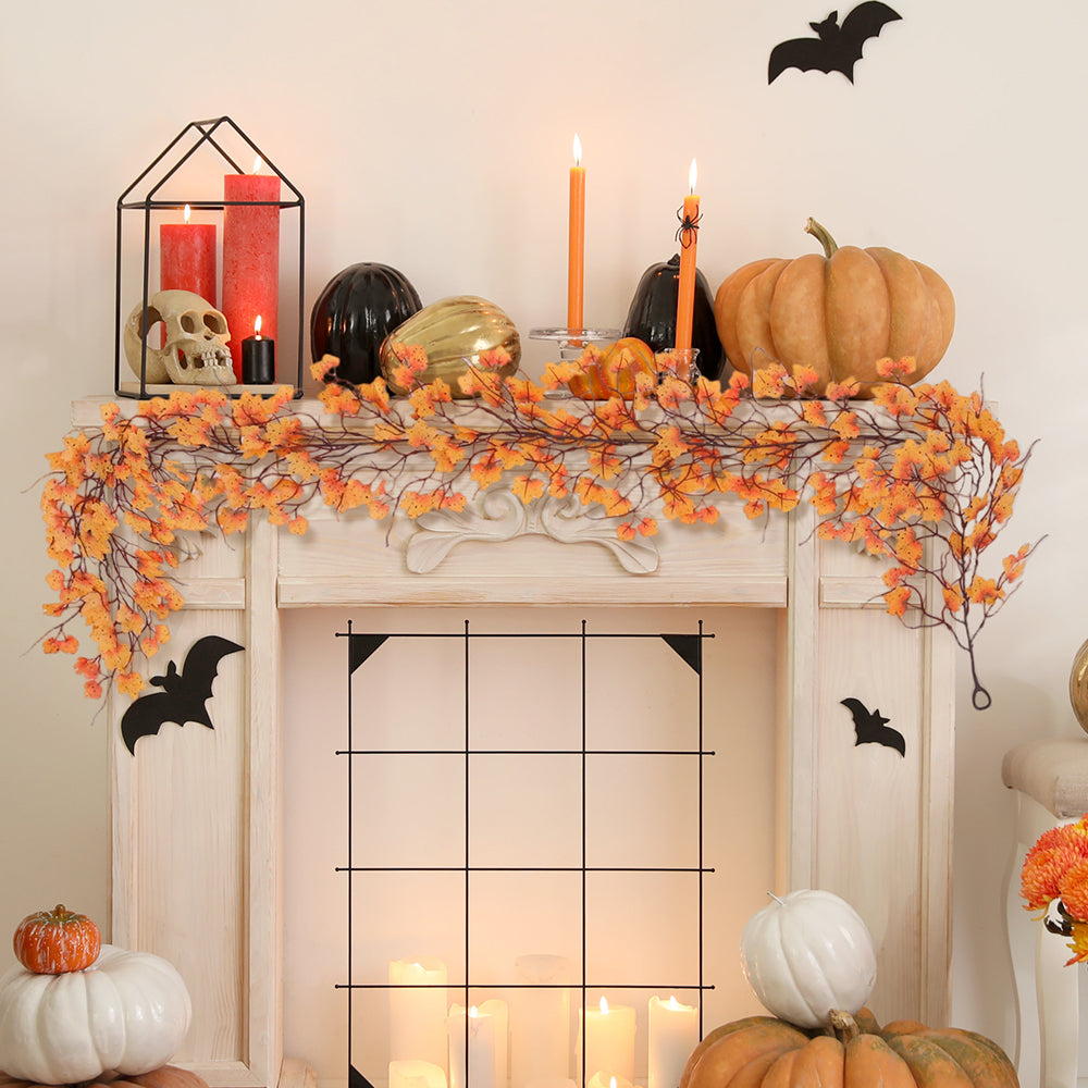 Orange maple leaf garland draped along a white mantelpiece with candles and pumpkins
