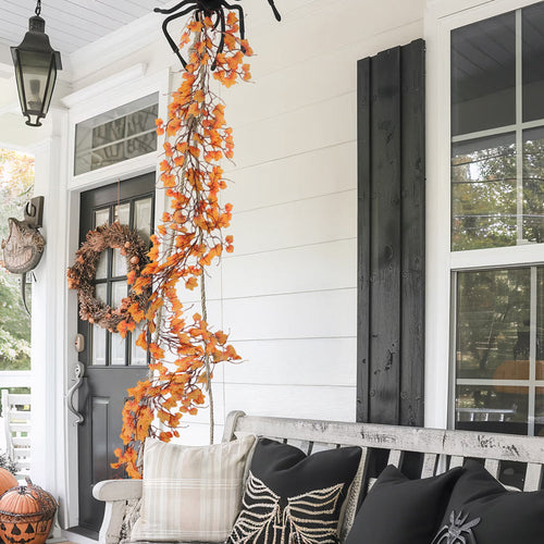 Orange maple leaf garland hanging down a white porch column beside a front door