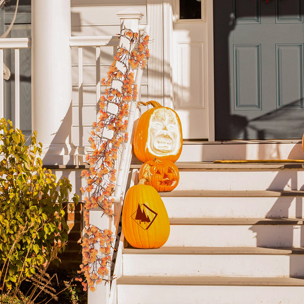Orange maple leaf garland wound along a porch stair rail next to carved pumpkins