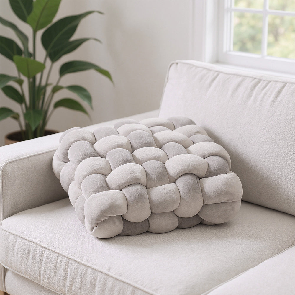 Grey knotted plush seat cushion on a cream sofa by a window