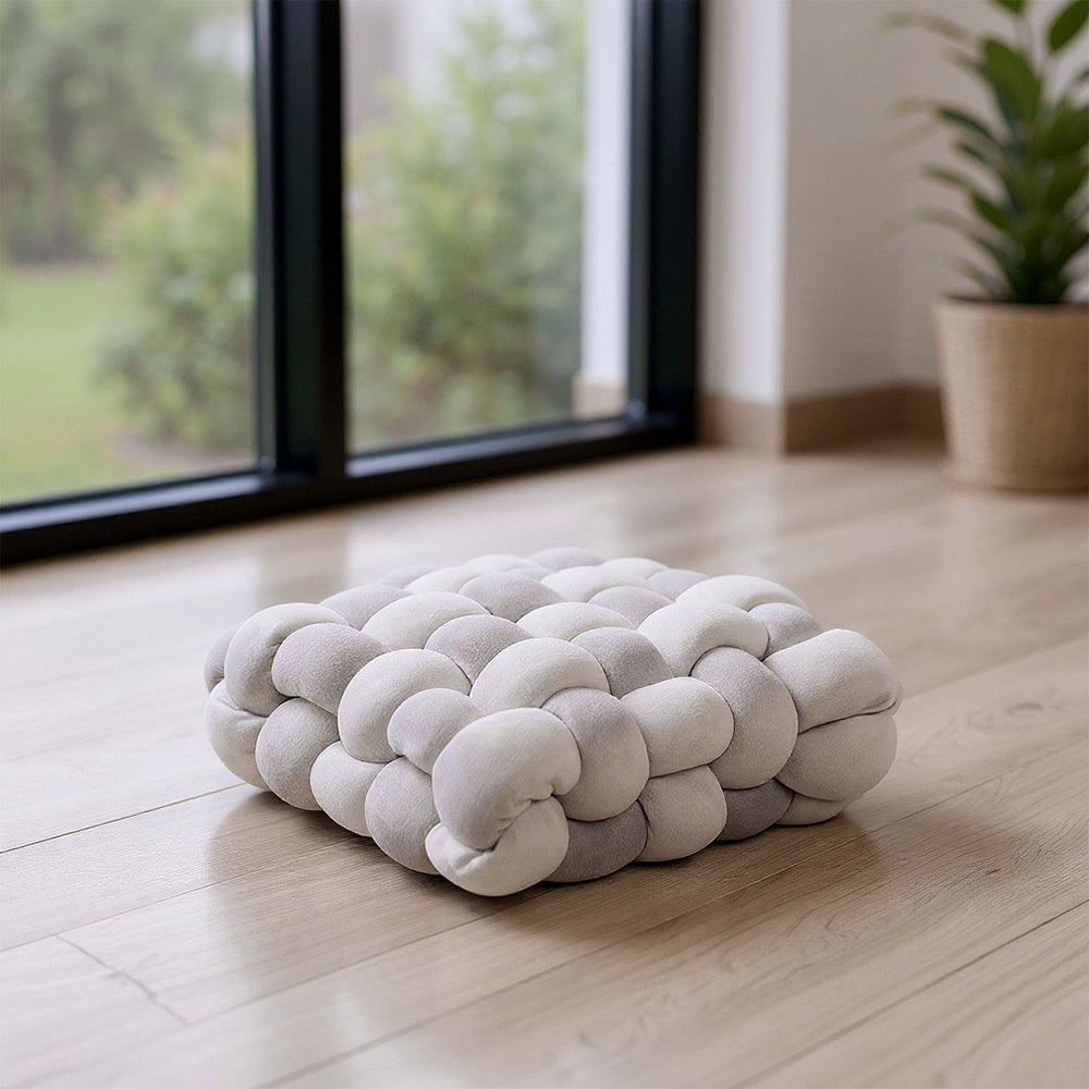 Grey knotted seat cushion on a wooden floor in front of tall windows
