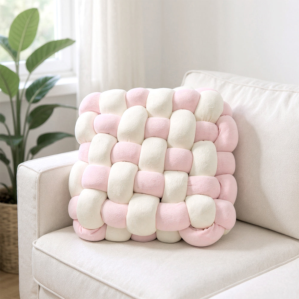 Cream and pink knotted cushion standing against the back of a white armchair