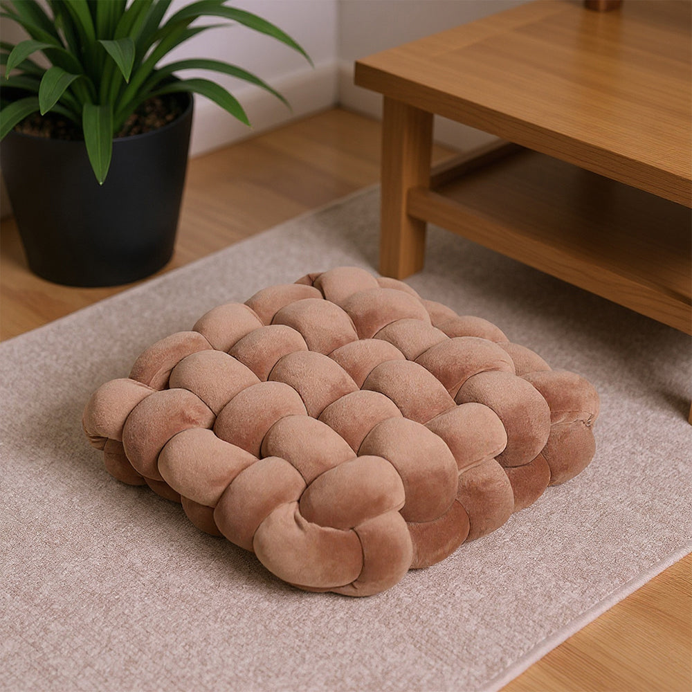 Caramel brown knotted seat cushion on a pink rug beside a wooden table