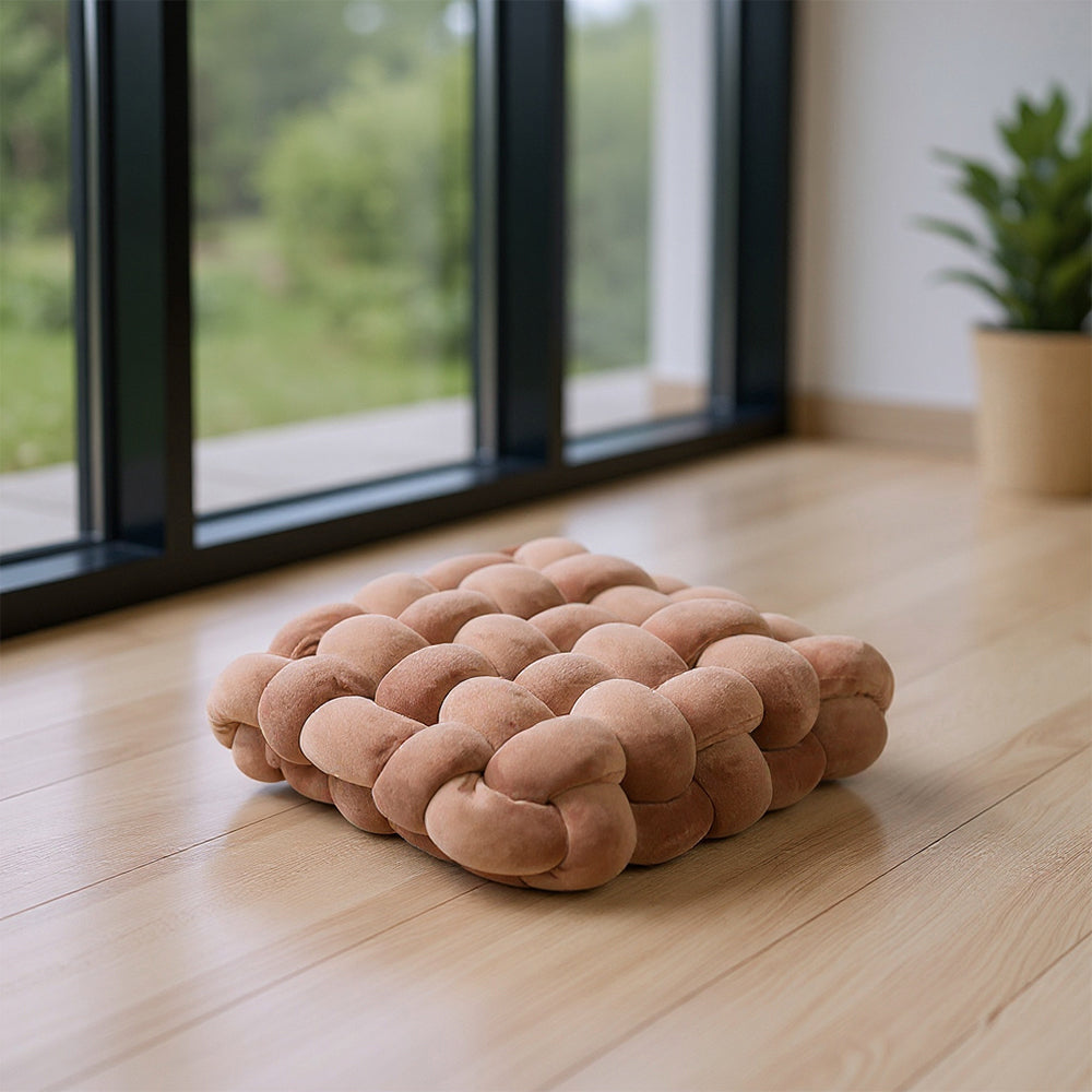 Caramel brown knotted seat cushion on a wooden floor by tall windows