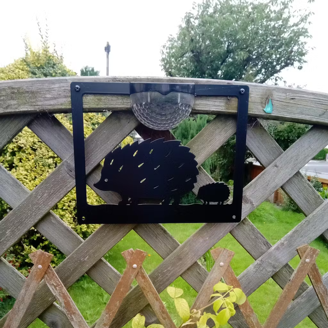 Open hedgehog cut-out solar plaque fixed to a wooden trellis fence in a garden