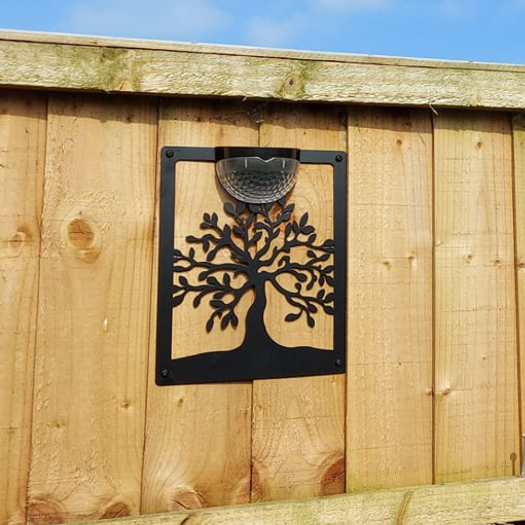 Open black tree of life cut-out solar plaque fixed to a wooden fence