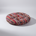 Round tufted seat cushion in a red, navy and cream geometric print on a grey background