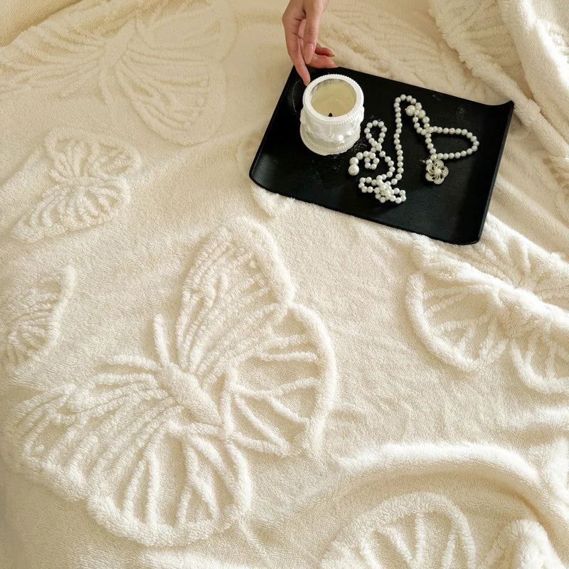 Cream fleece blanket with raised butterflies and a black tray holding a candle and pearls