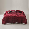 Thick wine red quilted plush blanket with a cream edge spread on a bed