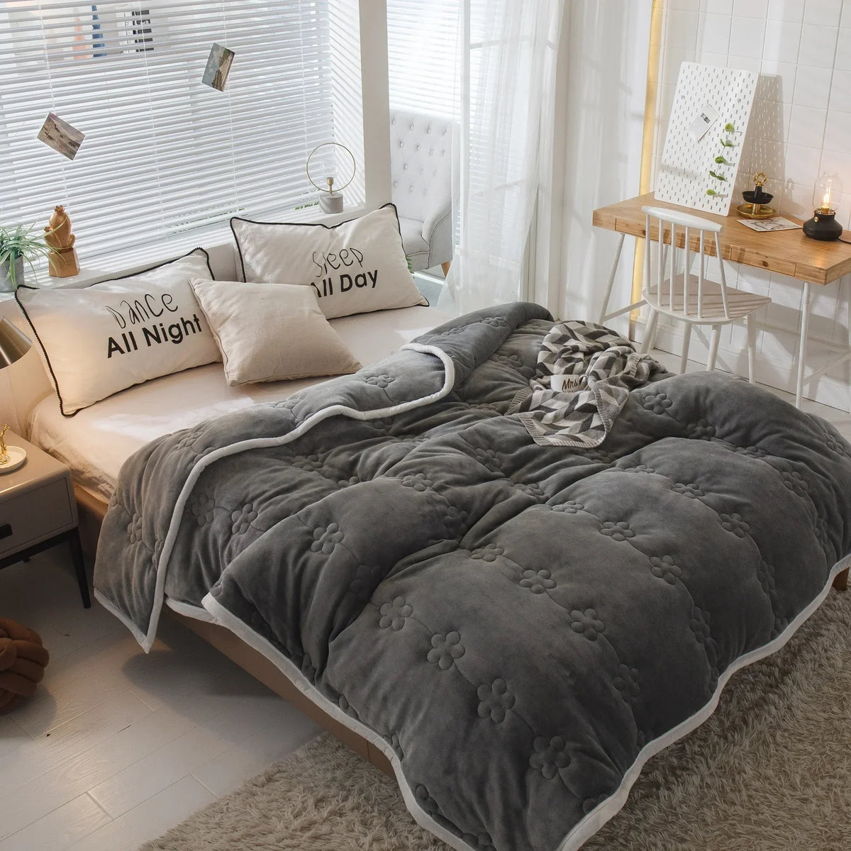 The grey version of the quilted blanket on a bed in a bright bedroom