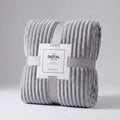 Light grey ribbed plush throw rolled up in a grey paper band on a pale background