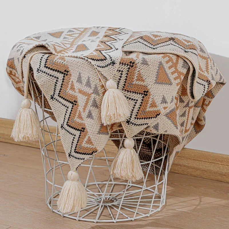 The knitted throw draped over a round wire basket with its tassels hanging