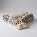 Beige knitted throw with a geometric diamond and zigzag pattern and cream corner tassels, folded