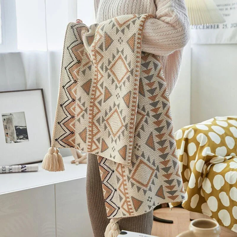 A person holding up the knitted throw to show its geometric pattern