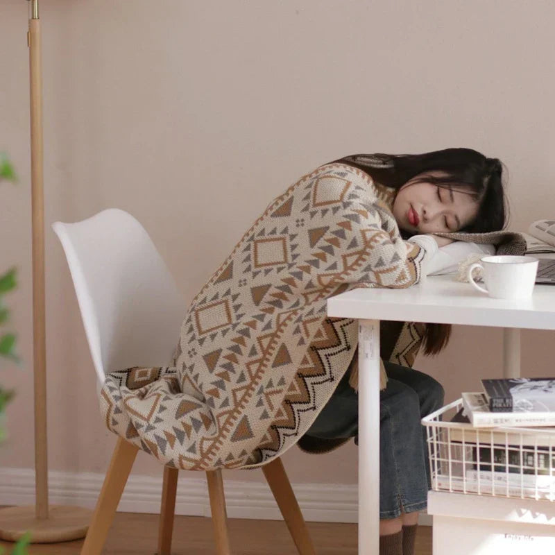 The geometric knitted throw wrapped around a person resting at a white desk