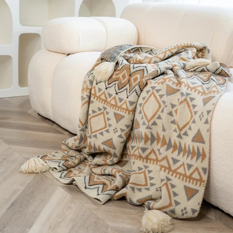 The beige geometric knitted throw draped from a white sofa onto the floor
