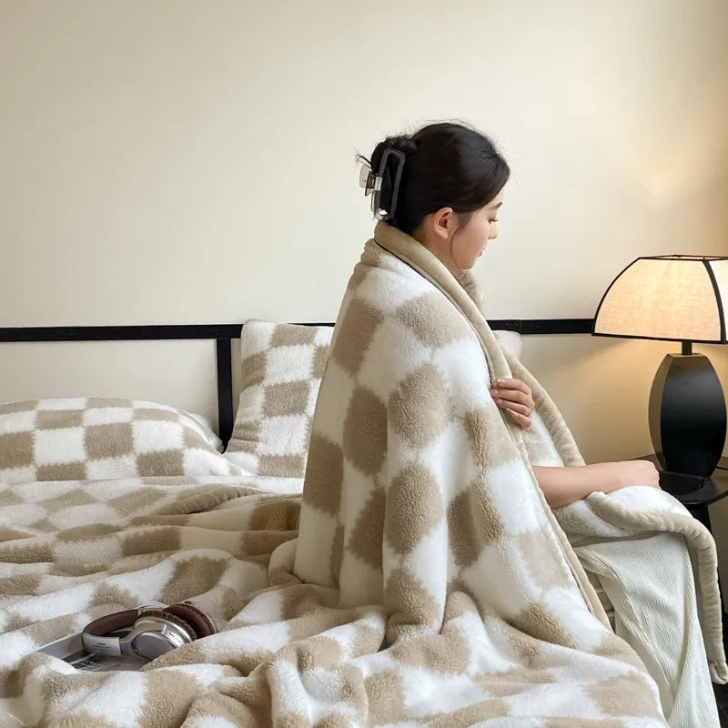 A woman sitting on a bed wrapped in the khaki and white checked blanket