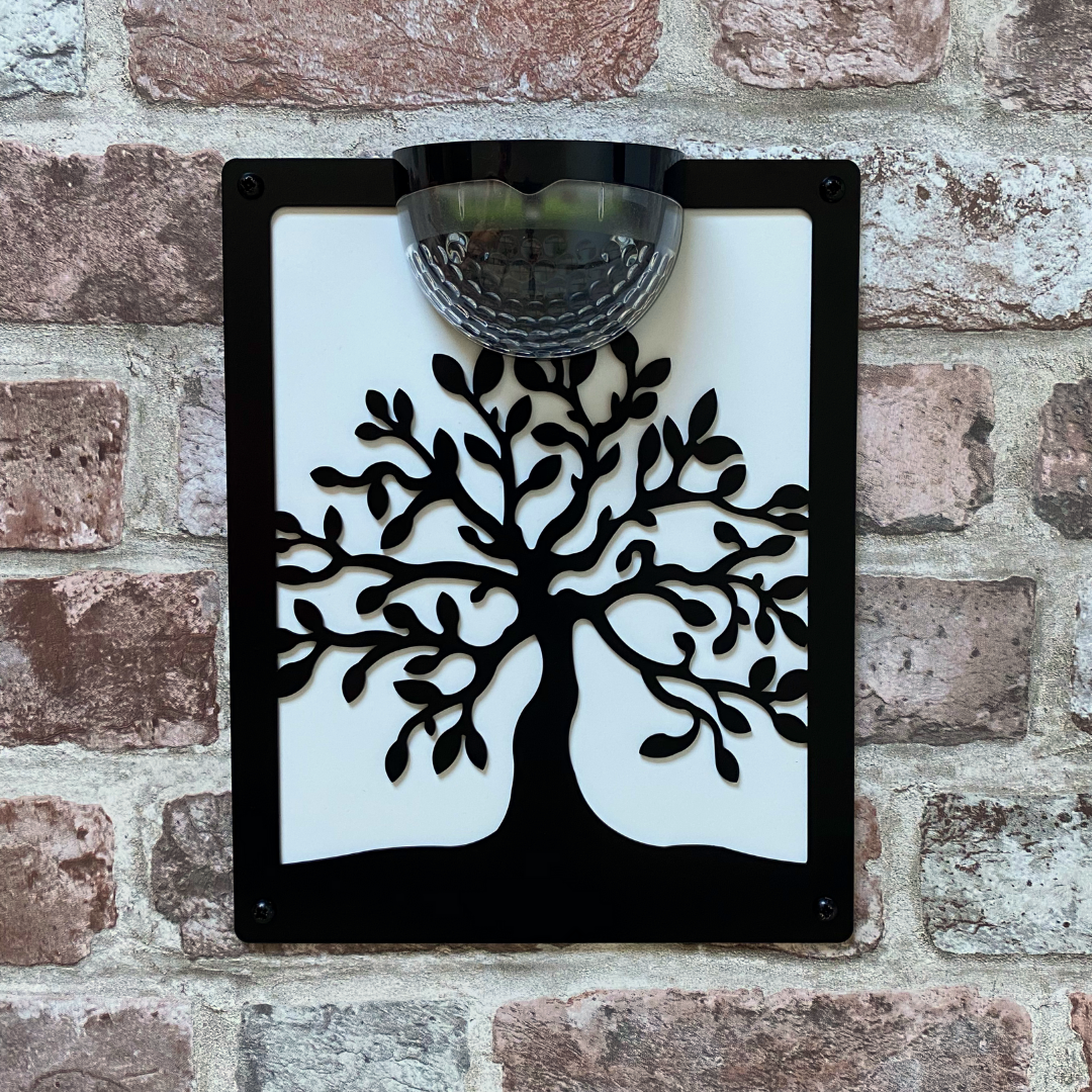 Tree of life solar plaque with white backing panel on a pale brick wall