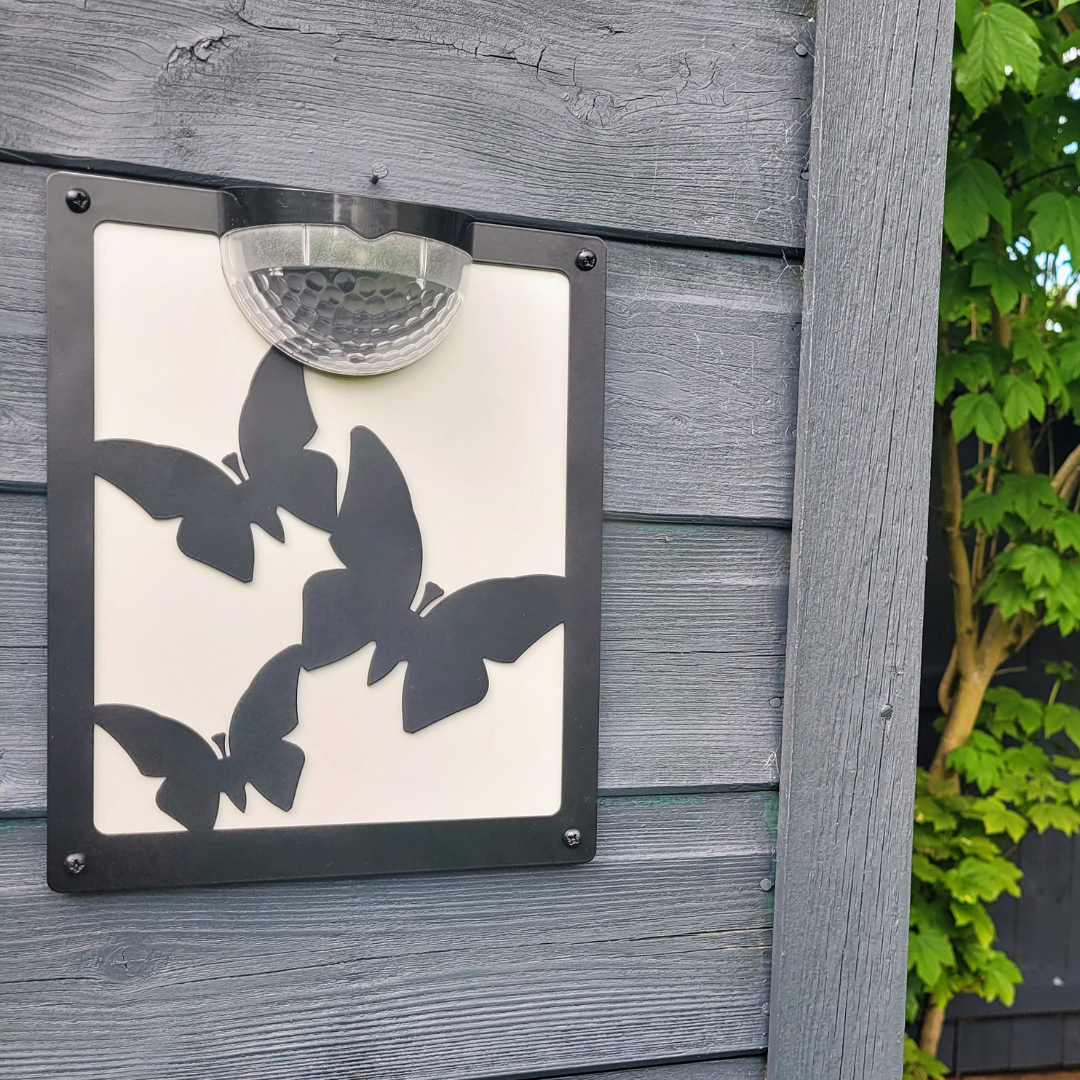 Butterfly solar plaque with white backing panel on grey wooden cladding