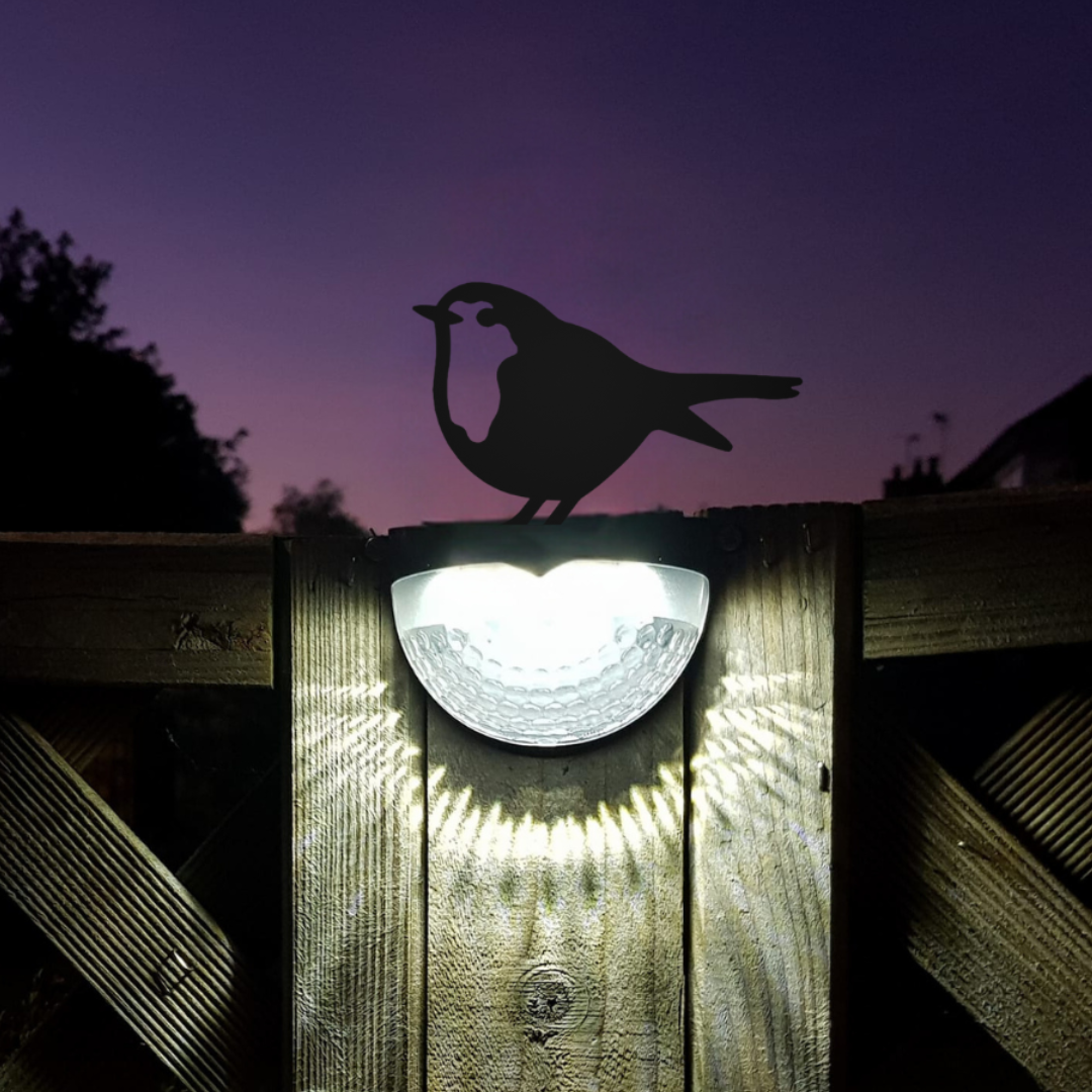 Two robin solar lights glowing white at dusk on a fence, facing each other