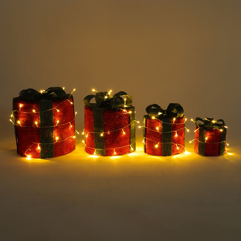 Four lit red sisal gift box decorations with green bows in a row, from large to small