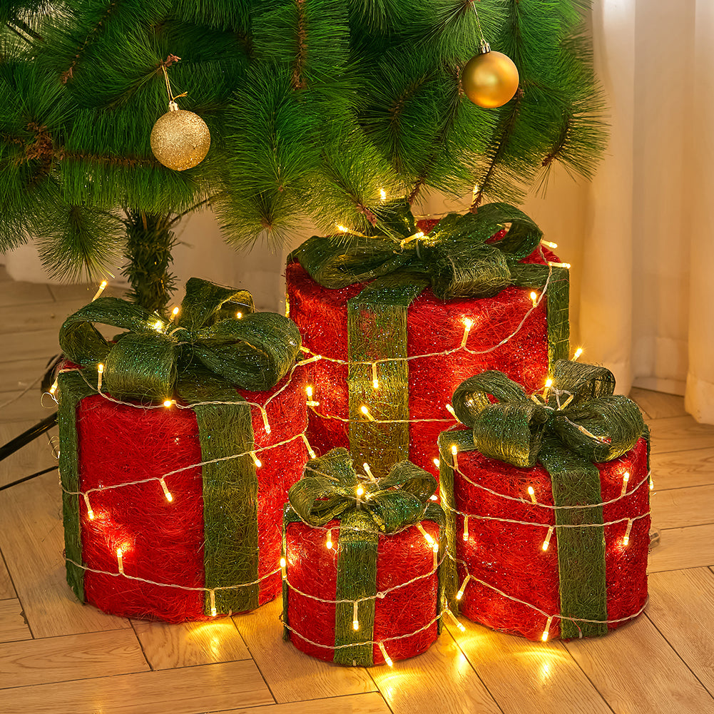 Four red sisal gift box decorations with green bows and LED lights under a Christmas tree