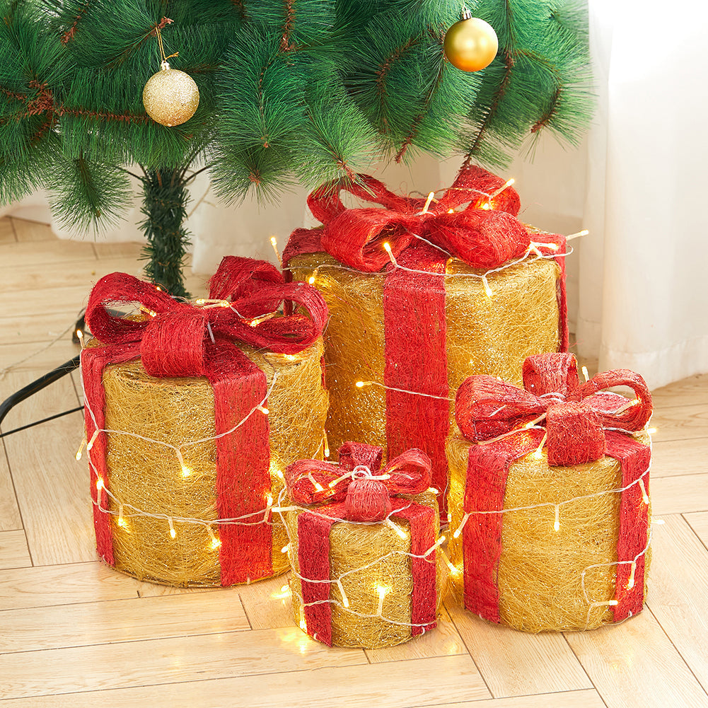 Four gold sisal gift box decorations with red bows and LED lights under a Christmas tree