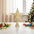 Gold glittered wire star tree topper standing on a table beside Christmas baubles