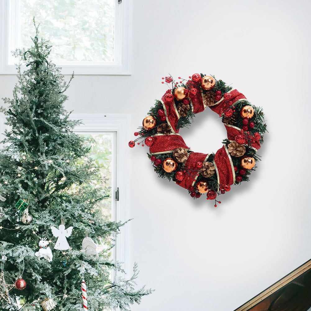 Christmas wreath with red glitter ribbon, gold baubles, pine cones and red berries on a white wall