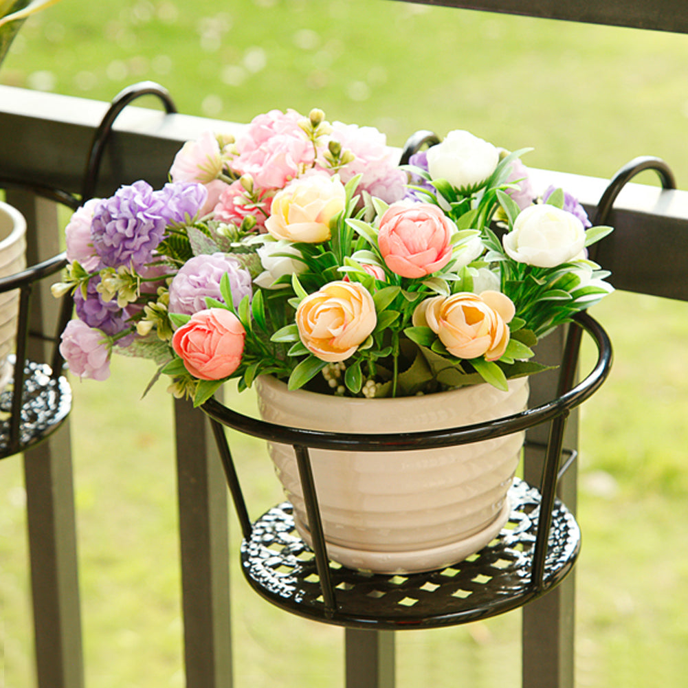 Black iron railing pot holder holding a pot of pink and peach roses on a garden railing