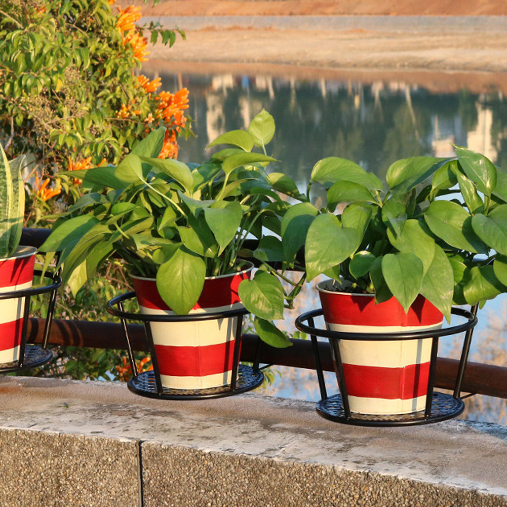Two iron pot holders with striped pots of green plants on a railing by a lake