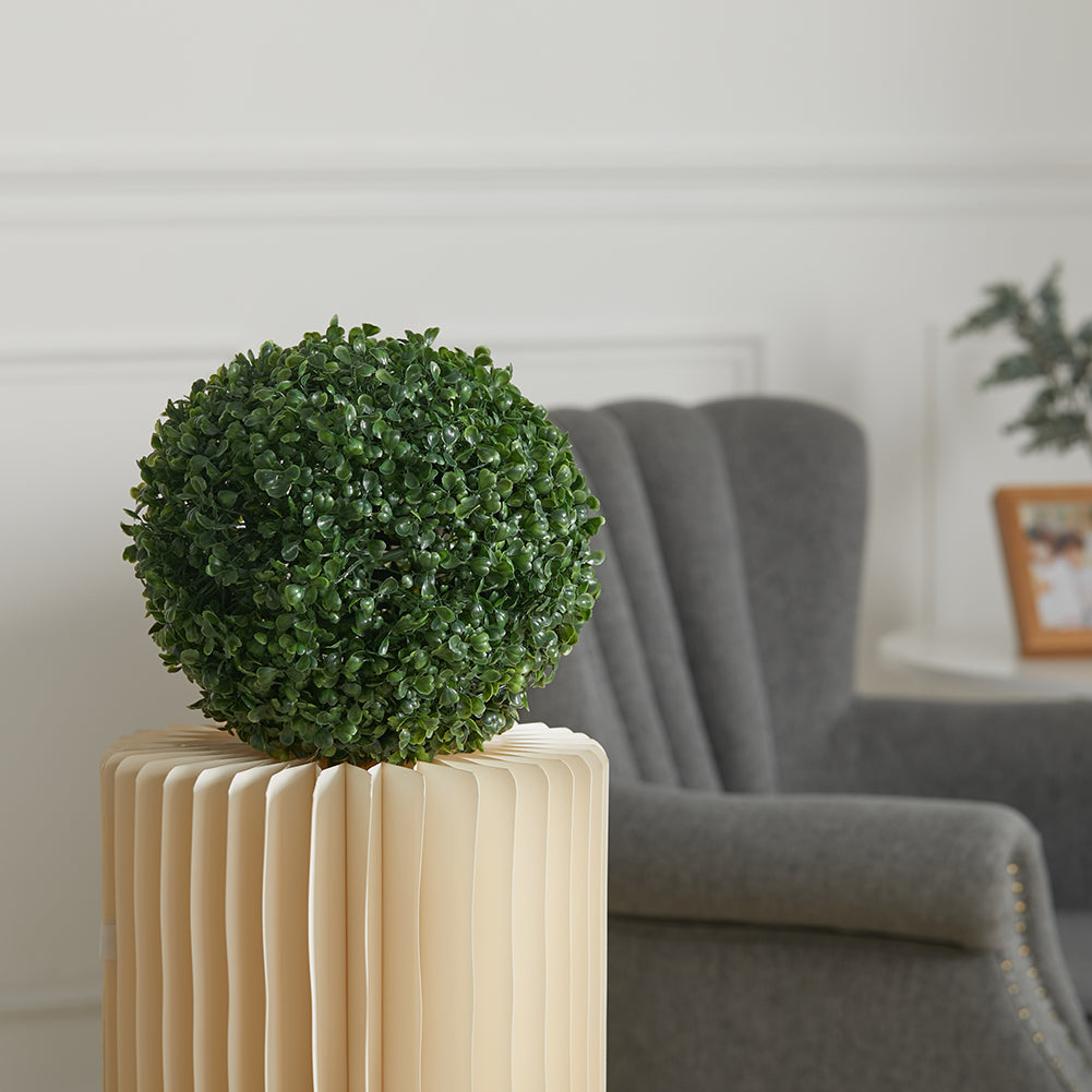 Artificial boxwood ball on a cream pleated pot beside a grey armchair