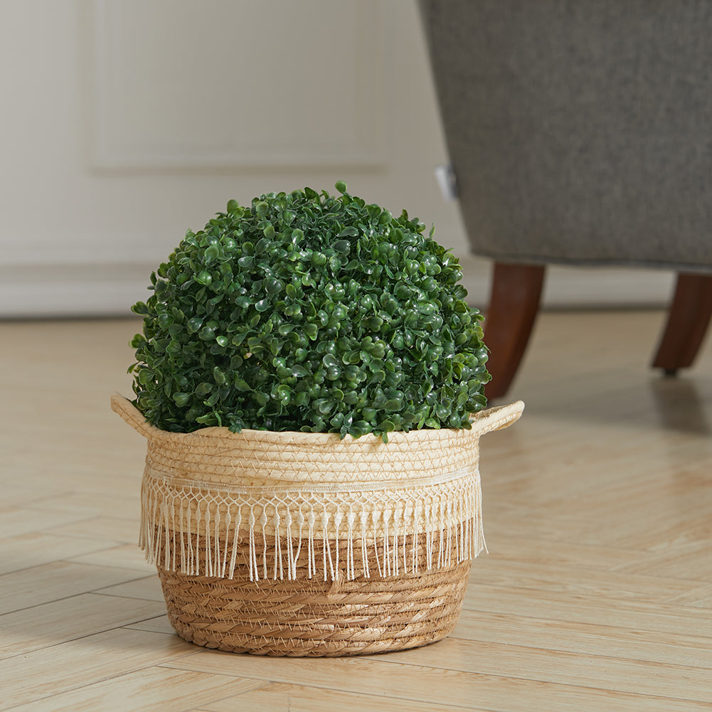 Artificial boxwood ball sitting in a woven seagrass basket with a fringed trim on a wooden floor
