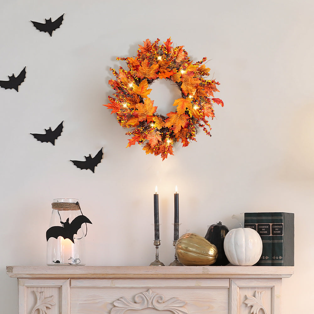 Autumn maple leaf wreath with lights on a cream wall above a sideboard with candles and pumpkins