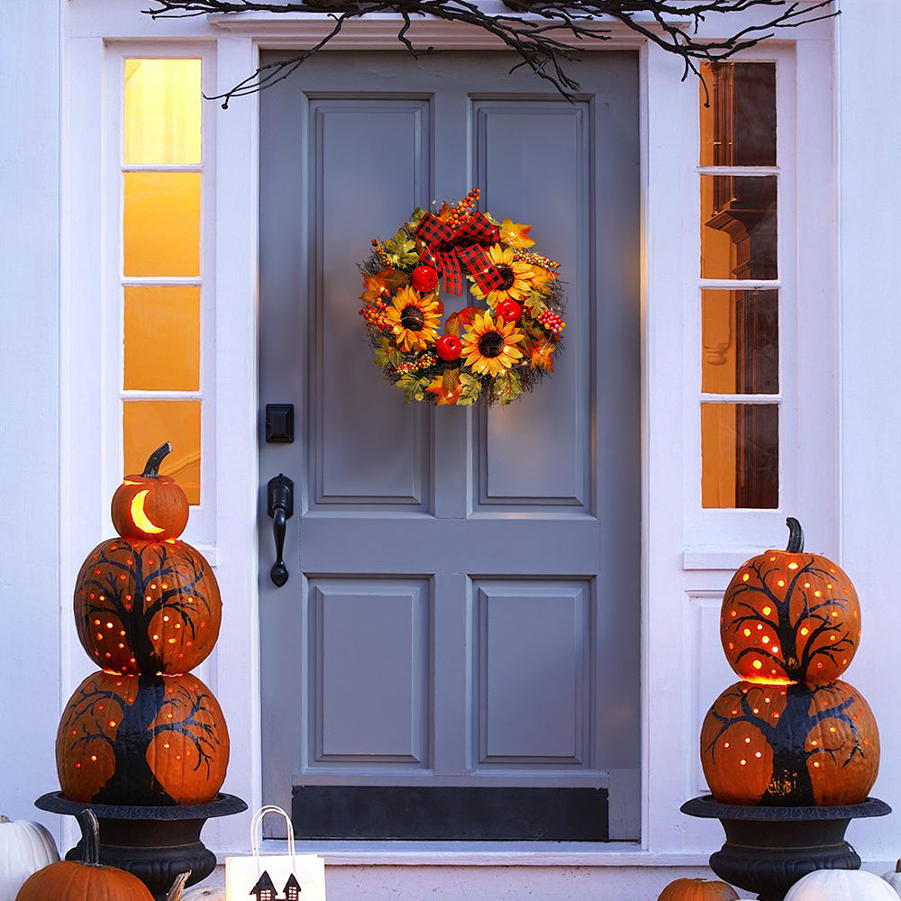 Sunflower and maple leaf wreath on a grey front door between carved pumpkin towers