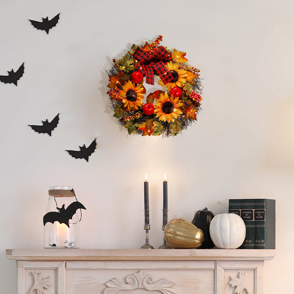 Autumn sunflower wreath with a plaid bow on a cream wall above a sideboard with candles and pumpkins