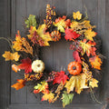 Autumn wreath of maple leaves, berries and small pumpkins hanging on a dark wooden door