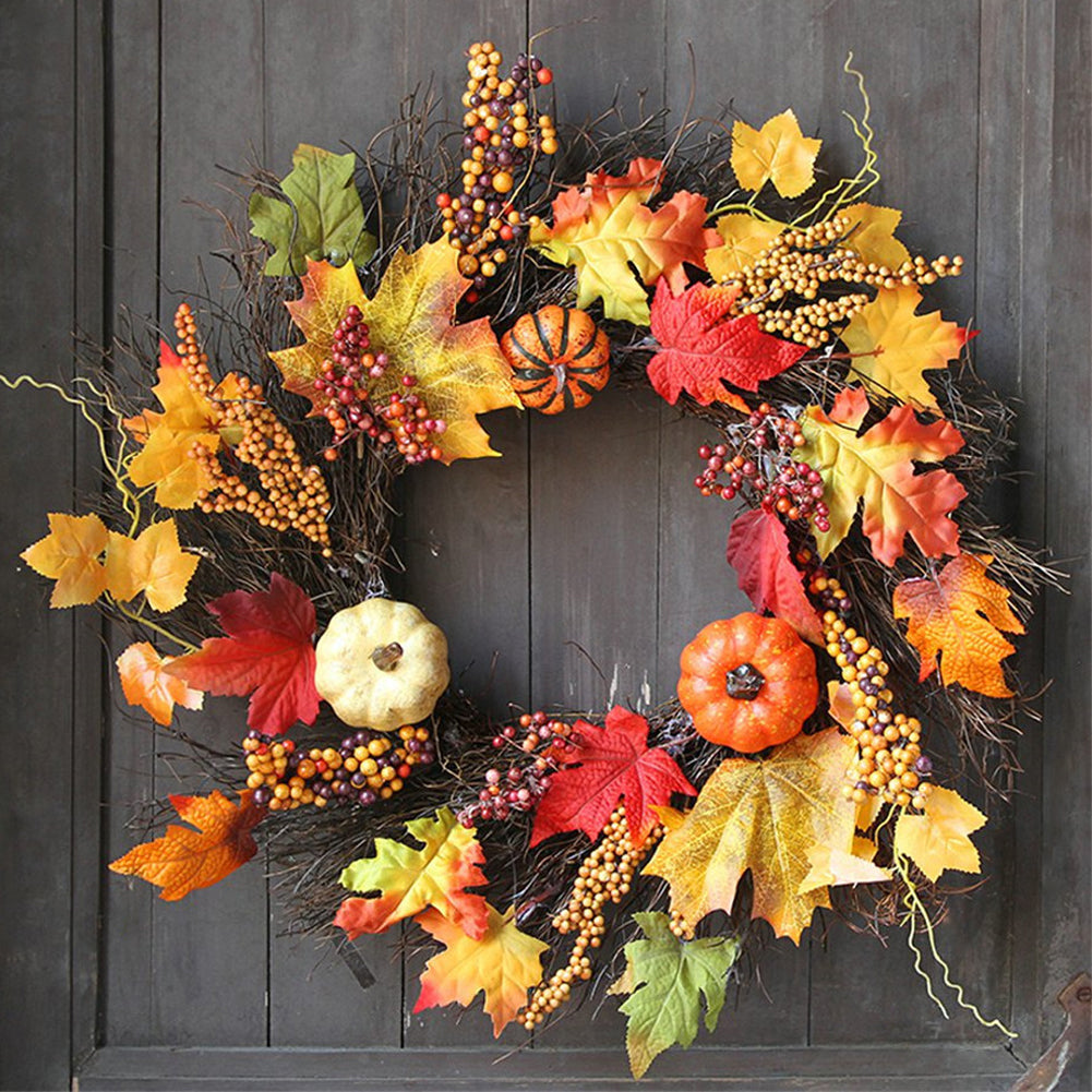 Autumn wreath of maple leaves, berries and small pumpkins hanging on a dark wooden door