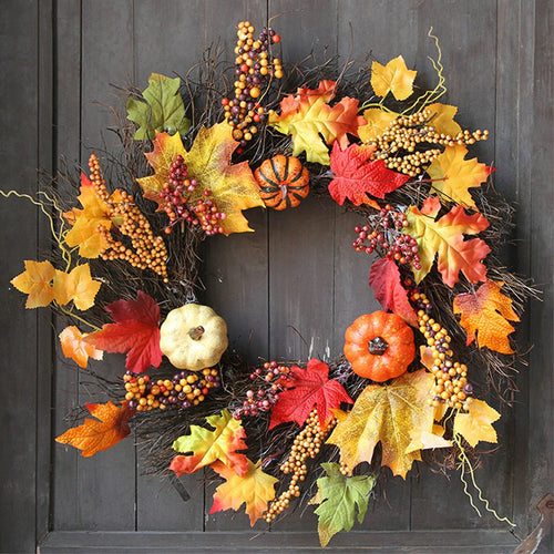 Autumn wreath of maple leaves, berries and small pumpkins hanging on a dark wooden door