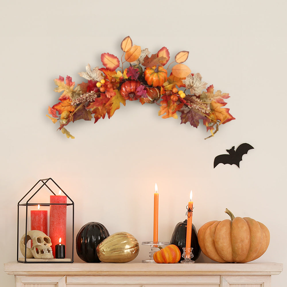 Arched autumn swag of maple leaves, pumpkins and berries on a pale wall above a shelf with candles