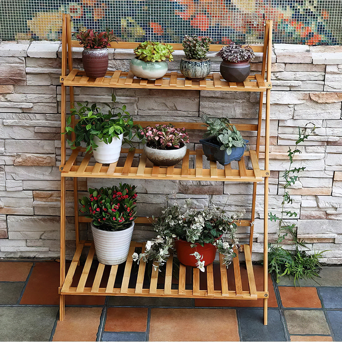 Ladder plant stand full of flowering pot plants in front of a stone wall