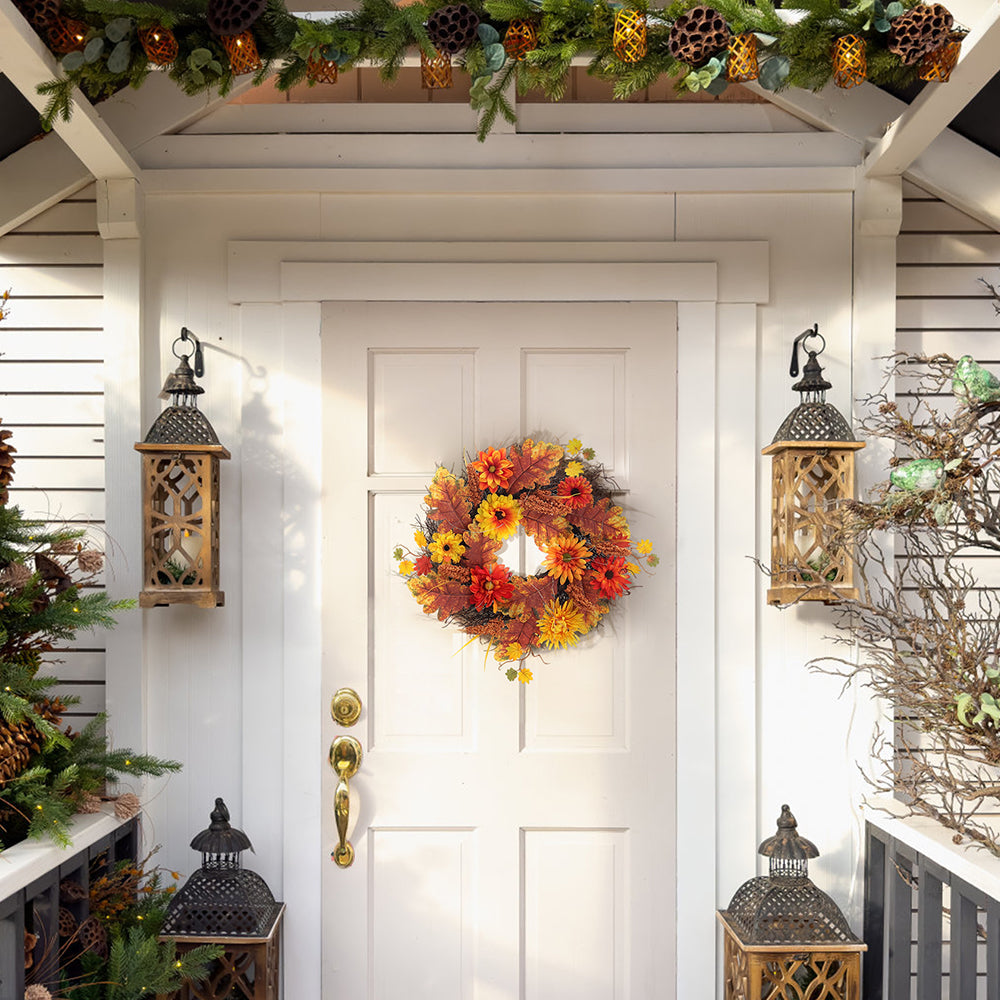 The daisy and maple leaf wreath on a white front door between two lanterns