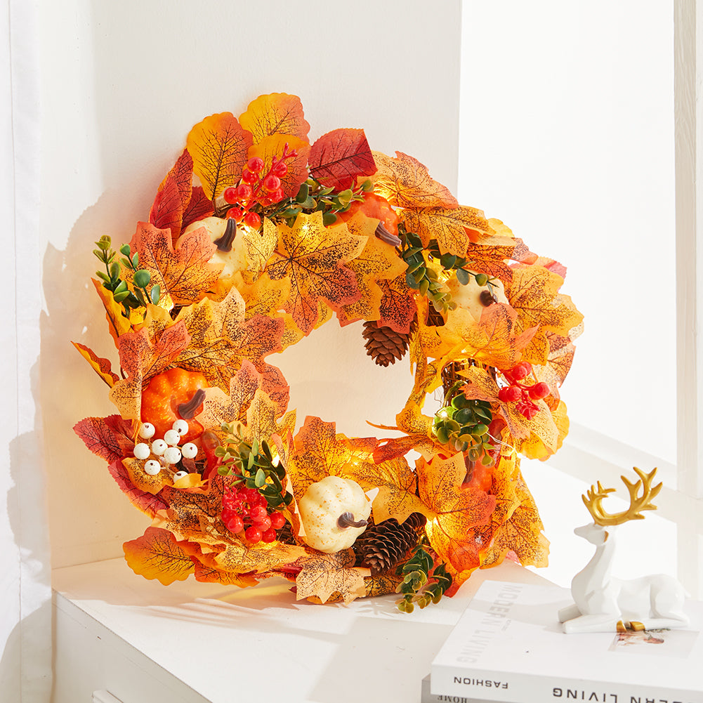The white and orange pumpkin wreath with its lights on beside a small deer figure