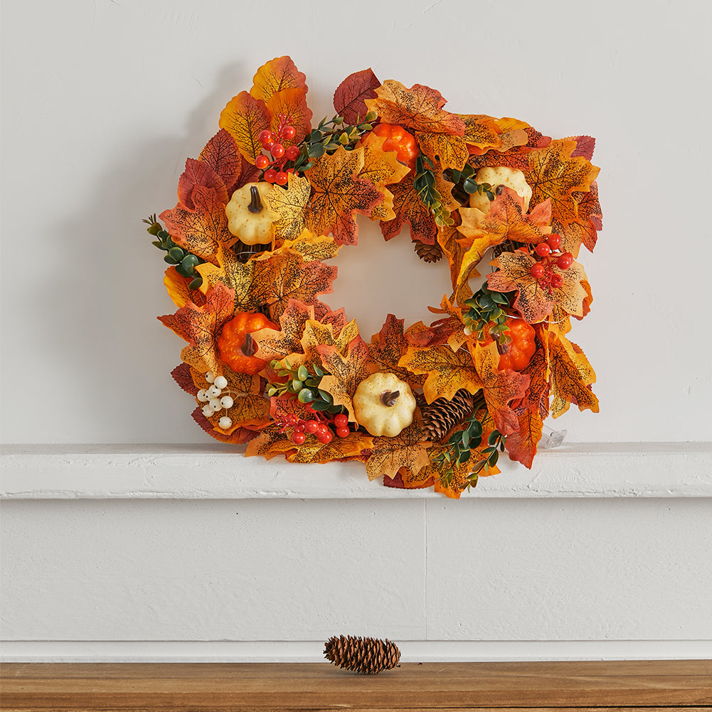 The pumpkin wreath hanging on a pale wall above a white shelf